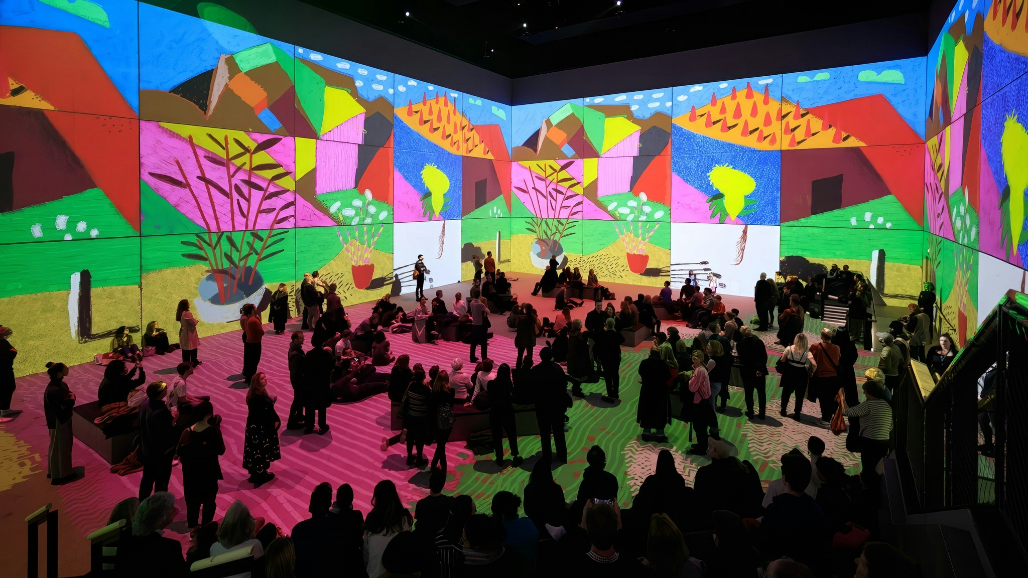 Visitors viewing immersive David Hockney digital art exhibit, "Bigger & Closer," in a vibrant gallery.