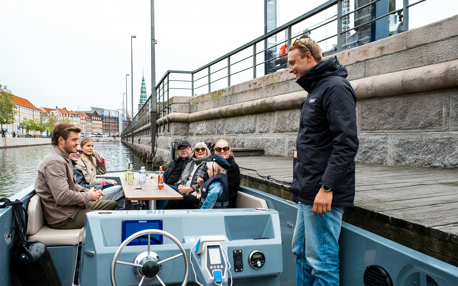 Guests on electric boat tour in Copenhagen, captain pedaling through scenic waterways.