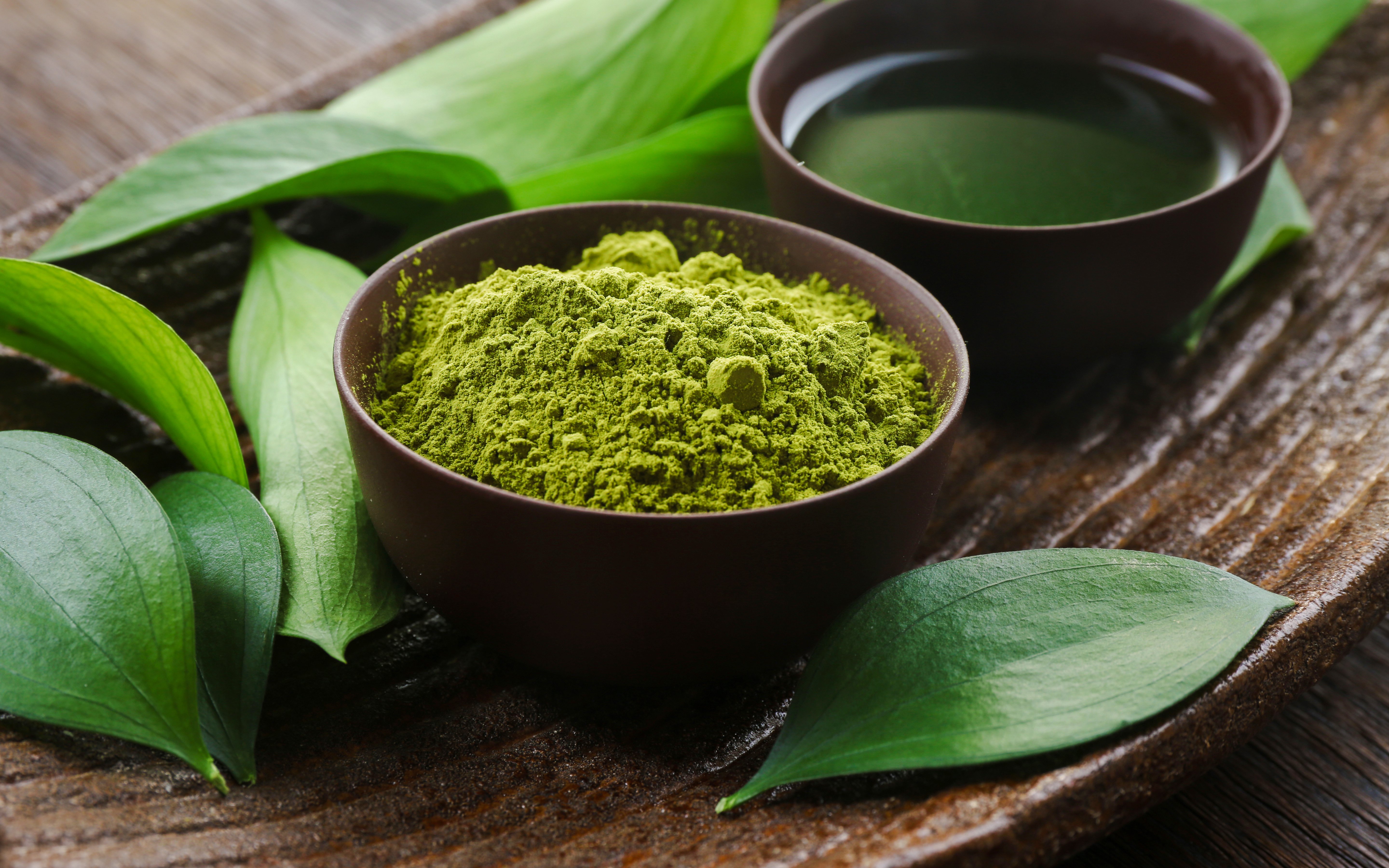 Bowl of matcha tea powder and leaves on a brown plate.