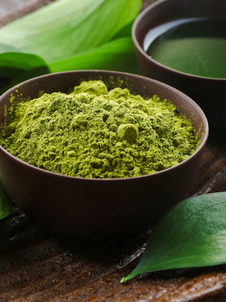 Bowl of matcha tea powder and leaves on a brown plate.