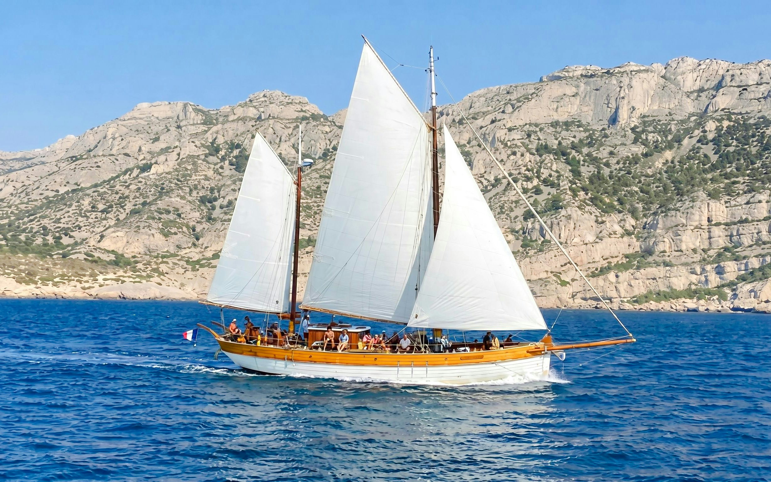 Sailing boat near Frioul Archipelago with rocky cliffs in the background.