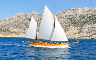 Sailing boat near Frioul Archipelago with rocky cliffs in the background.