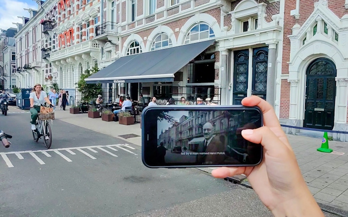 Mobile screen showing Anne Frank tour content in Amsterdam street scene.