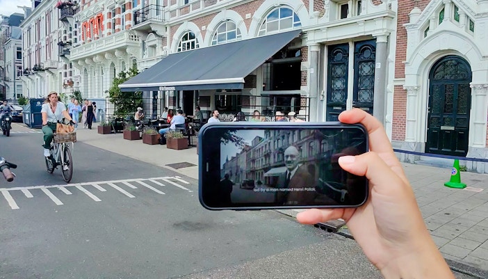 Mobile screen showing Anne Frank tour content in Amsterdam street scene.