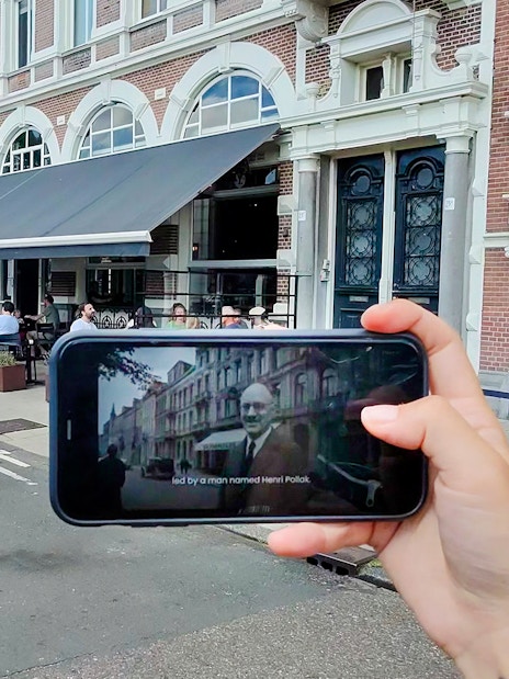 Mobile screen showing Anne Frank tour content in Amsterdam street scene.