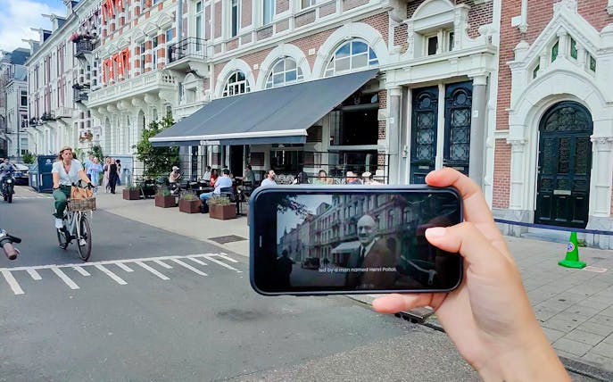 Mobile screen showing Anne Frank tour content in Amsterdam street scene.