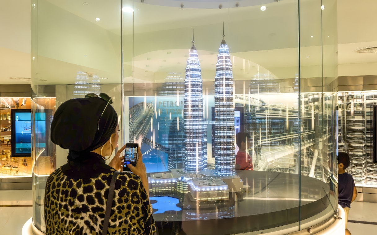 Visitor photographing Petronas Twin Towers model in Kuala Lumpur exhibit.