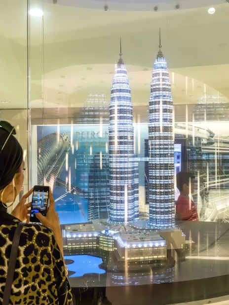 Visitor photographing Petronas Twin Towers model in Kuala Lumpur exhibit.