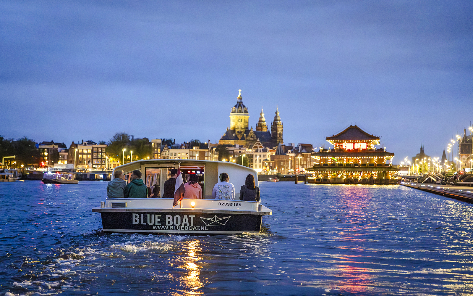 Winter evening cruise boat on Amsterdam canal with city lights and church in background.