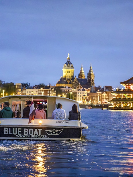 Winter evening cruise boat on Amsterdam canal with city lights and church in background.