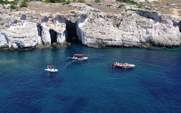 Boats near the grotto at Ortigia Island, Sicily, with rocky cliffs in the background.