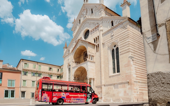 Red sightseeing bus in front of Verona Cathedral during City Sightseeing Verona Hop-on Hop-off Tour.