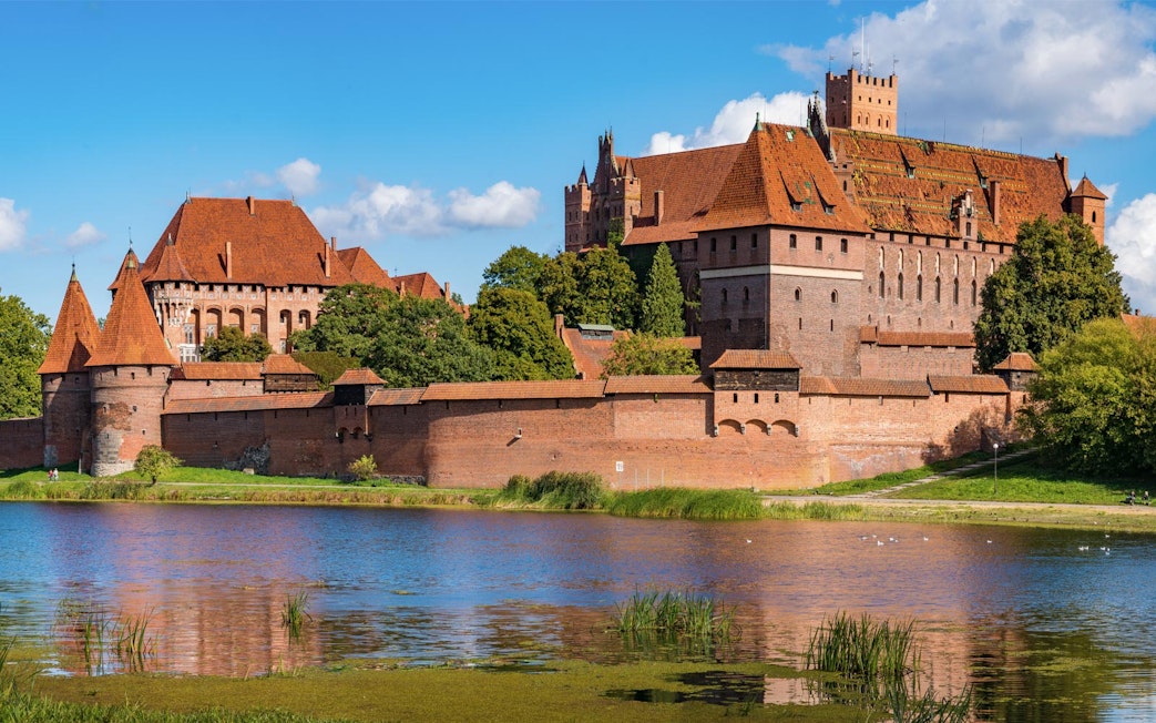 Malbork Castle with red brick walls and towers reflected in a river, Poland.
