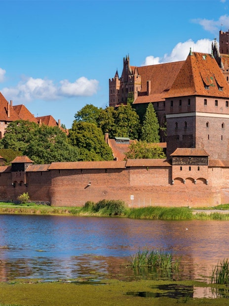 Malbork Castle with red brick walls and towers reflected in a river, Poland.