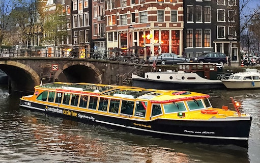 Canal cruise boat on Amsterdam canal with historic buildings in the background.