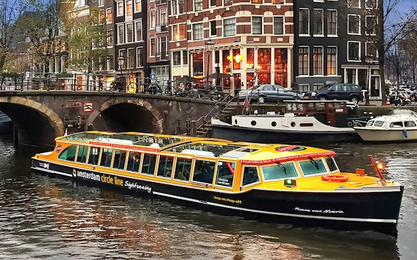 Canal cruise boat on Amsterdam canal with historic buildings in the background.
