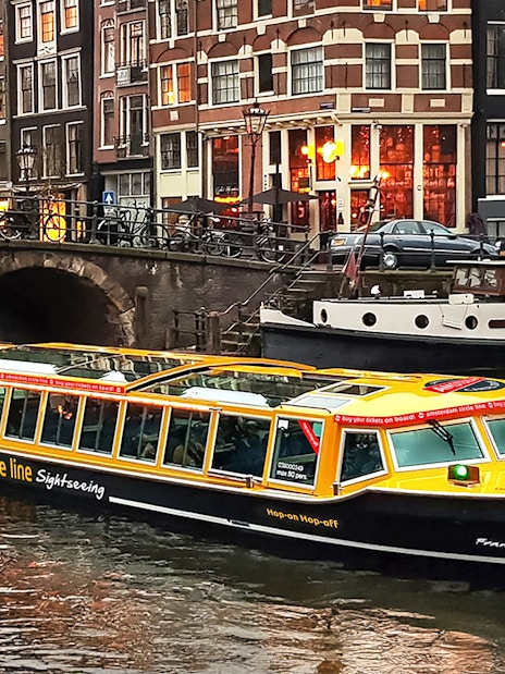 Canal cruise boat on Amsterdam canal with historic buildings in the background.