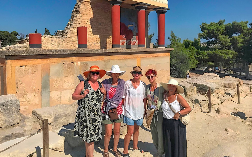 Guests exploring Knossos Palace ruins with frescoes and columns in Crete.