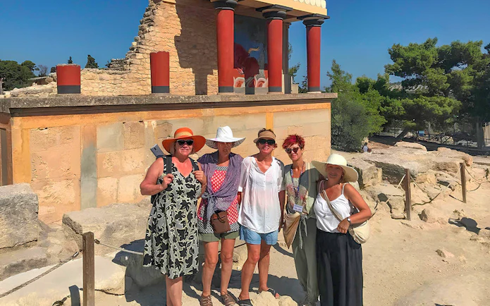 Guests exploring Knossos Palace ruins with frescoes and columns in Crete.