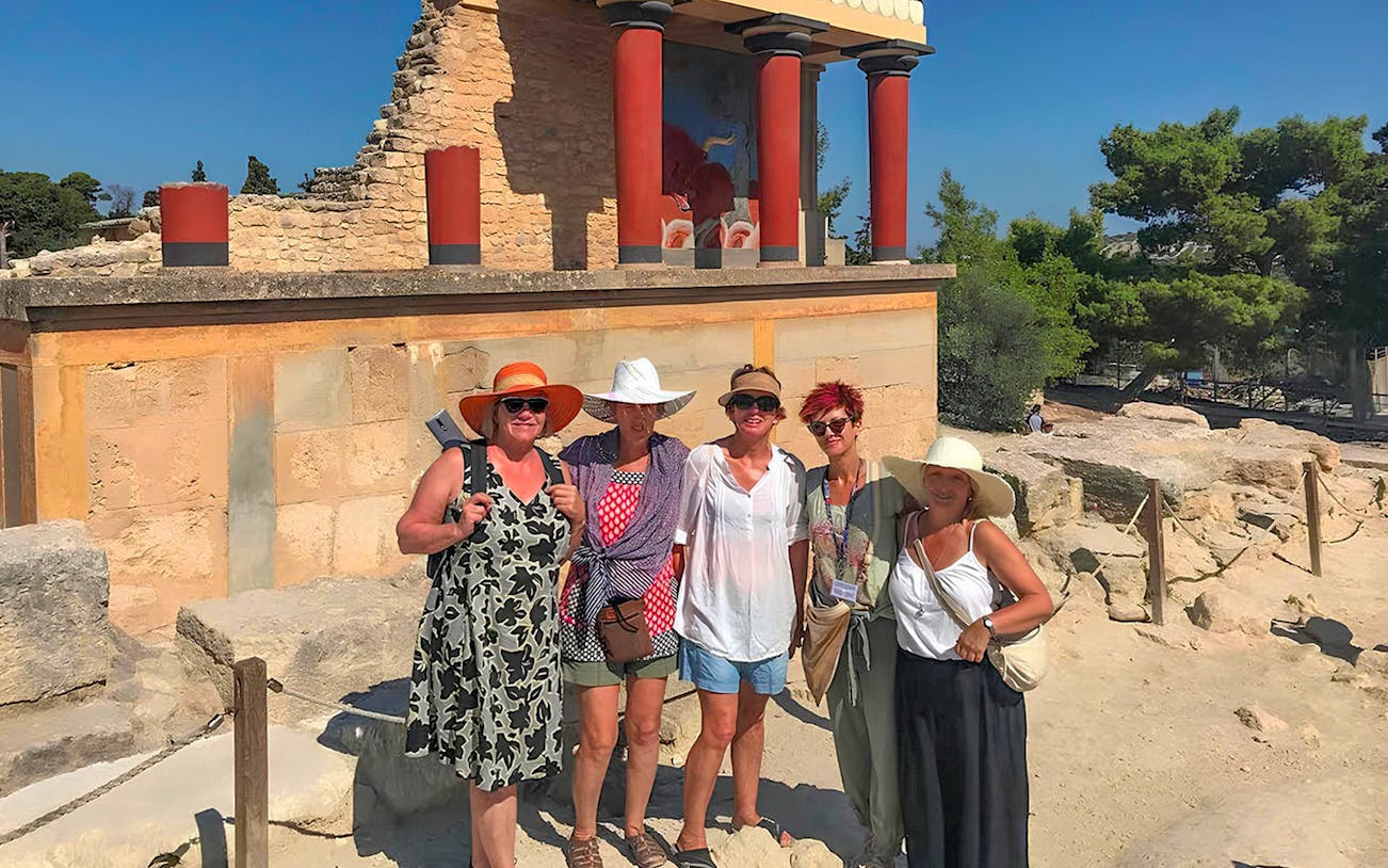Guests exploring Knossos Palace ruins with frescoes and columns in Crete.