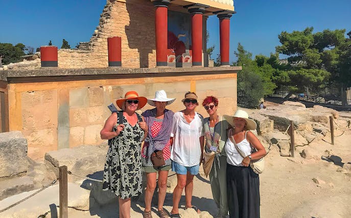 Guests exploring Knossos Palace ruins with frescoes and columns in Crete.