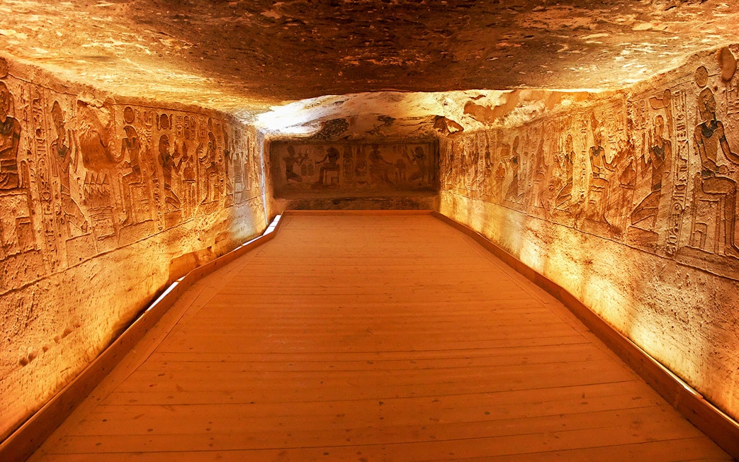Interior corridor of Abu Simbel Temple with ancient Egyptian carvings on illuminated walls.