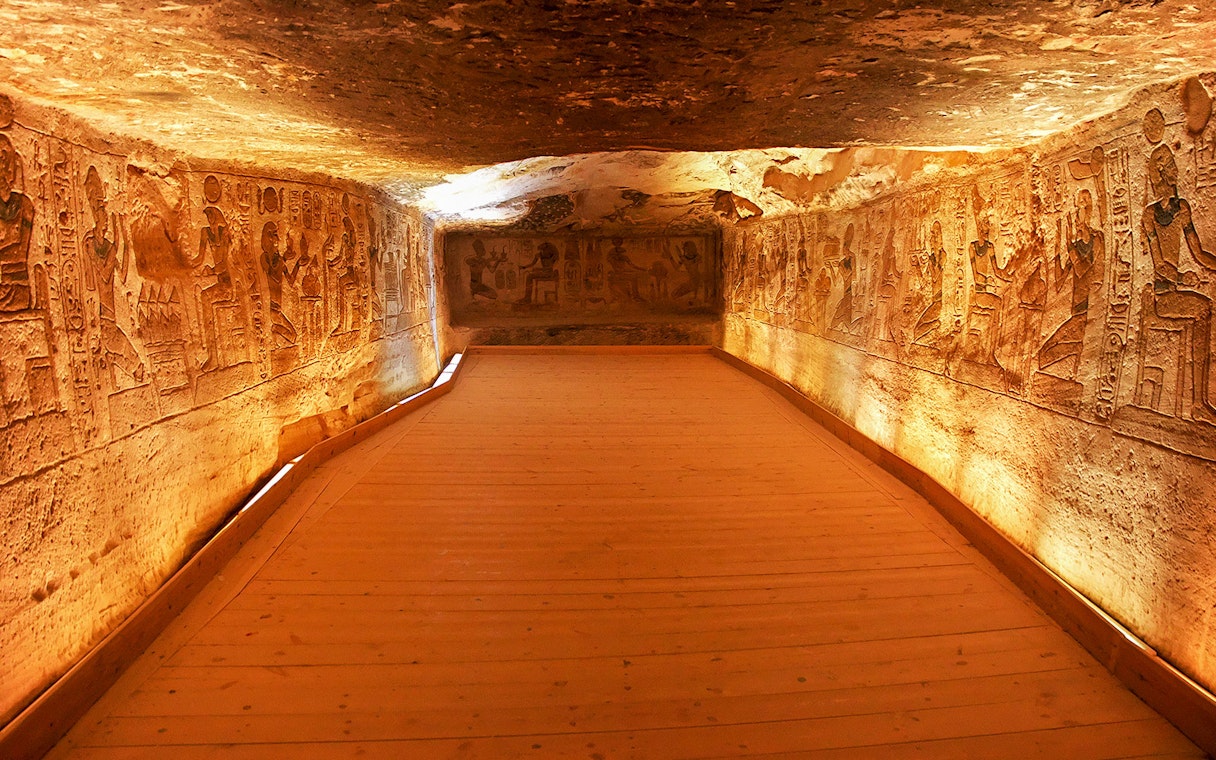 Interior corridor of Abu Simbel Temple with ancient Egyptian carvings on illuminated walls.
