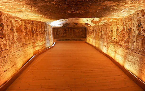 Interior corridor of Abu Simbel Temple with ancient Egyptian carvings on illuminated walls.