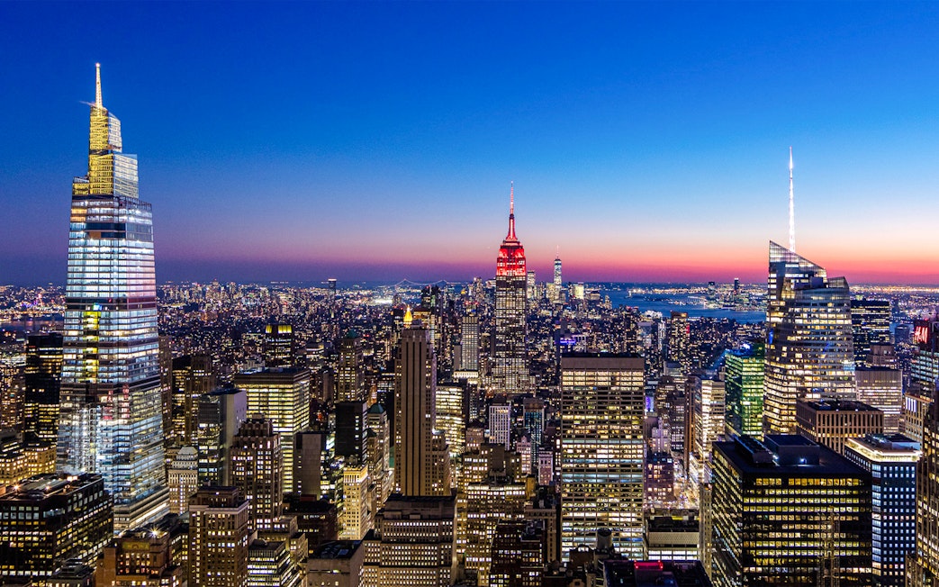 New York City skyline at night from SUMMIT One Vanderbilt, featuring illuminated skyscrapers.