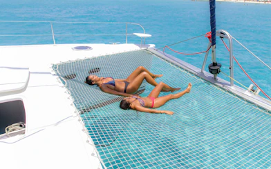 Relaxing on a catamaran net over turquoise water during Isla Mujeres tour.