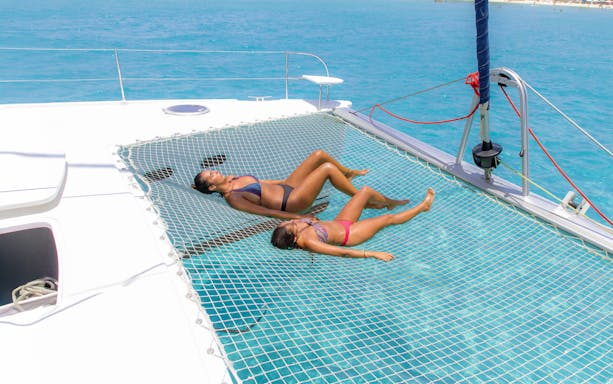 Relaxing on a catamaran net over turquoise water during Isla Mujeres tour.