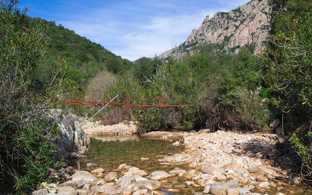 Trekking trail with a walking bridge leading to Piscina Irgas Waterfall, Cagliari, Italy.