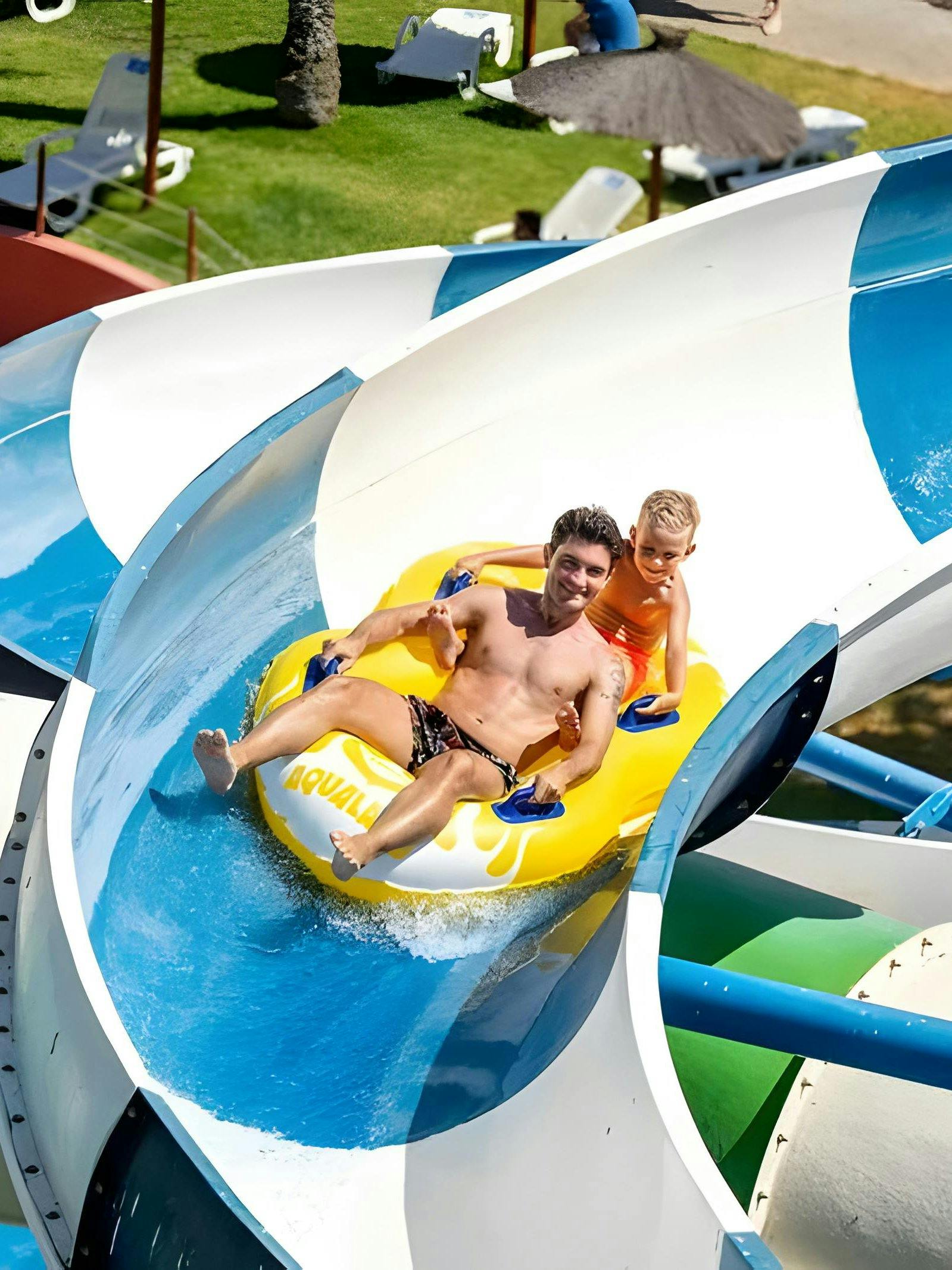 Father and son on a yellow raft sliding down a water slide at Aqualand Algarve.
