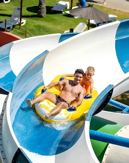 Father and son on a yellow raft sliding down a water slide at Aqualand Algarve.