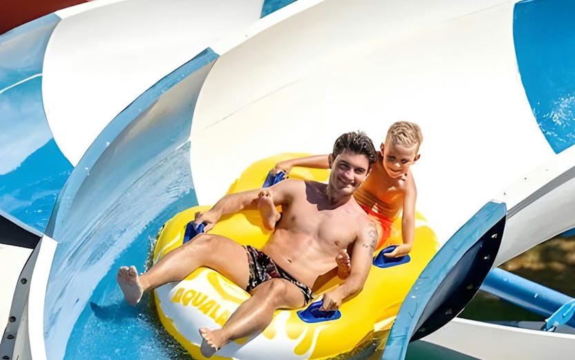 Father and son on a yellow raft sliding down a water slide at Aqualand Algarve.