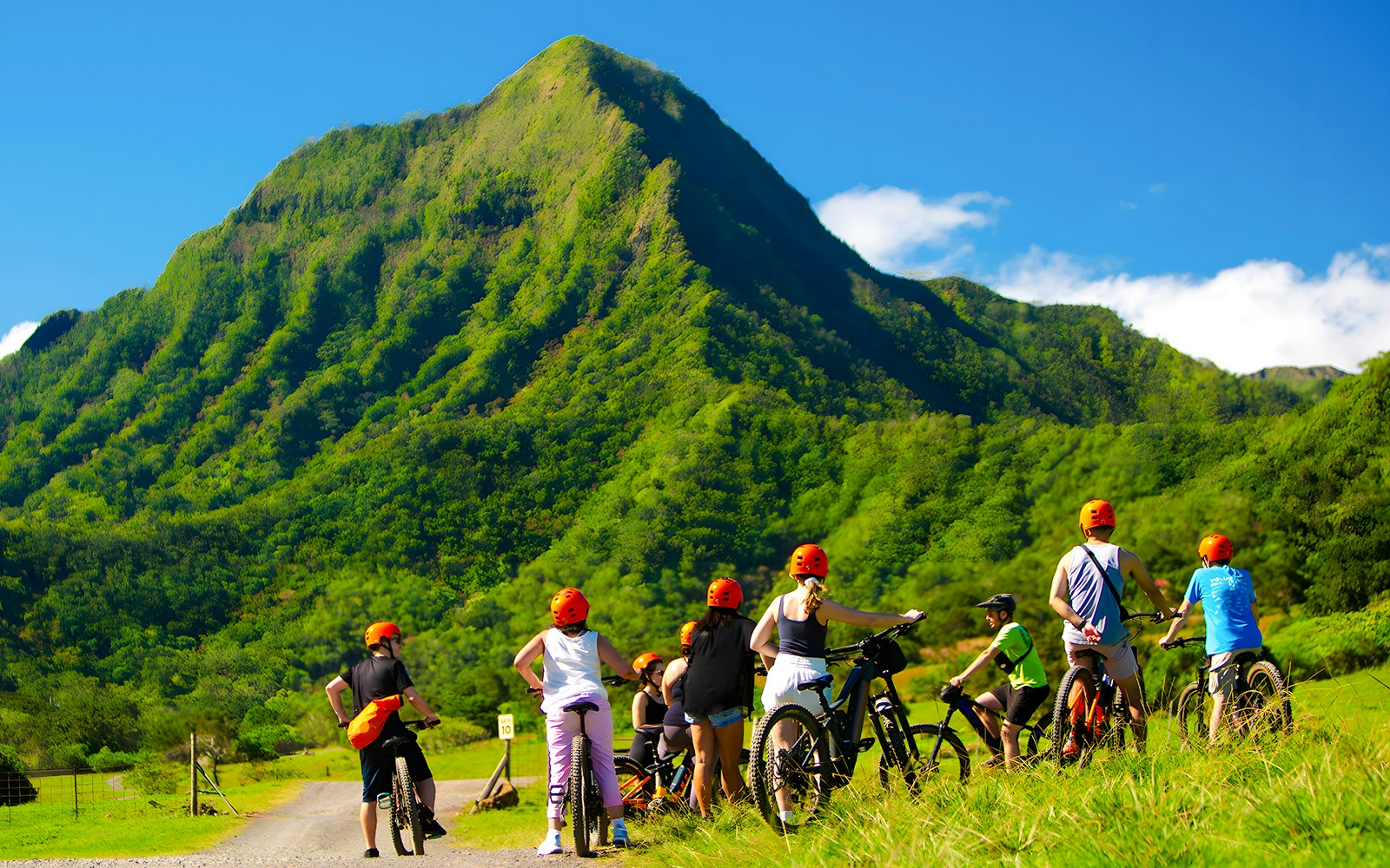 Novice riders on e-bikes at Kualoa Ranch with lush green mountains in the background.