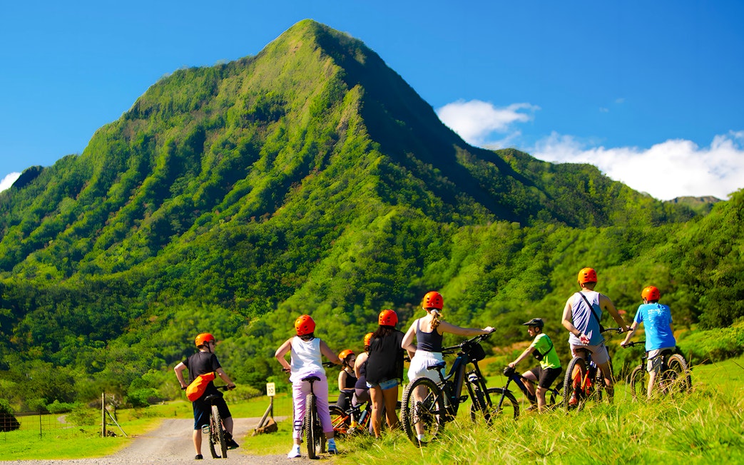 Novice riders on e-bikes at Kualoa Ranch with lush green mountains in the background.