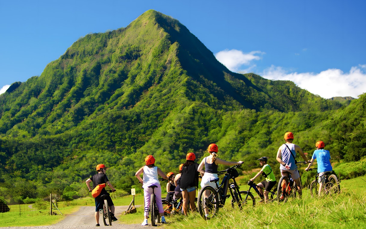 Novice riders on e-bikes at Kualoa Ranch with lush green mountains in the background.