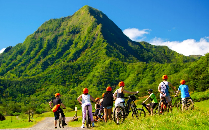 Novice riders on e-bikes at Kualoa Ranch with lush green mountains in the background.