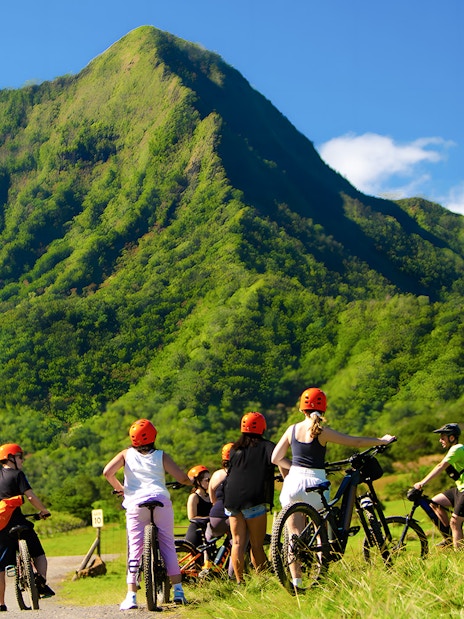 Novice riders on e-bikes at Kualoa Ranch with lush green mountains in the background.