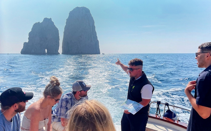 Tour group on boat near Faraglioni rocks, Capri, with guide pointing, part of Capri & Anacapri tour.