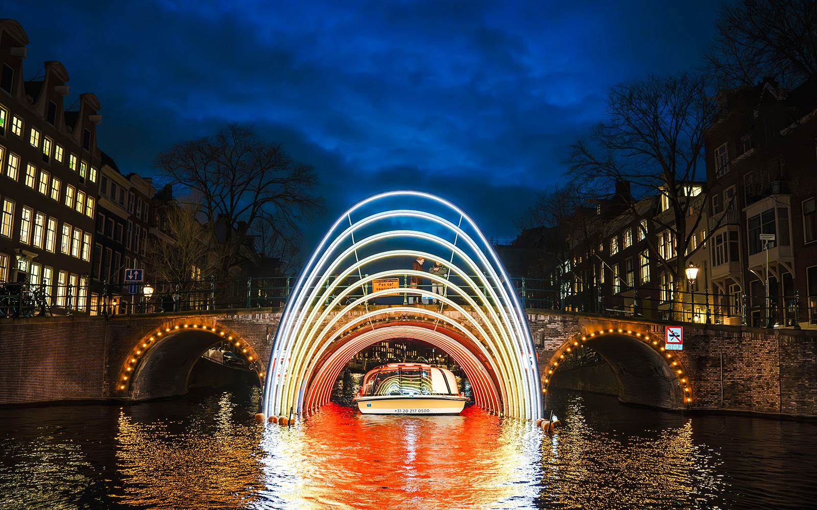 Amsterdam canal cruise passing under illuminated arches during Light Festival.