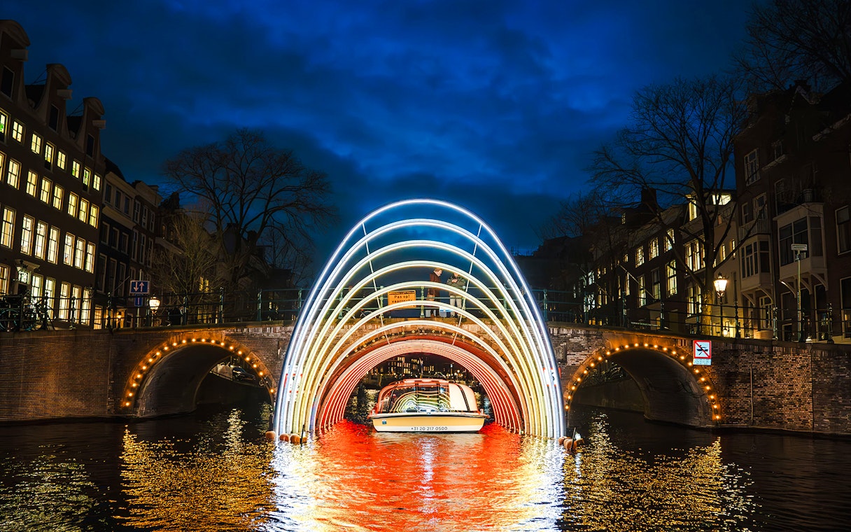 Amsterdam canal cruise passing under illuminated arches during Light Festival.