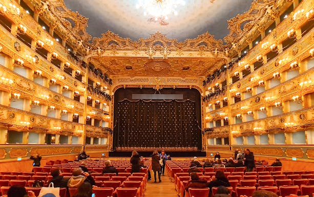 Teatro La Fenice interior with ornate balconies and stage curtain in Venice, Italy.