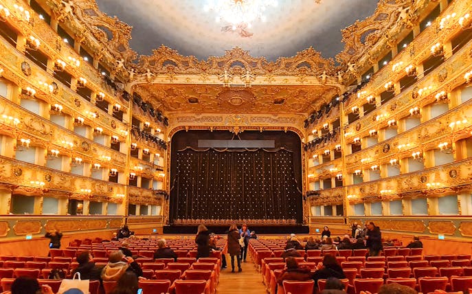 Teatro La Fenice interior with ornate balconies and stage curtain in Venice, Italy.