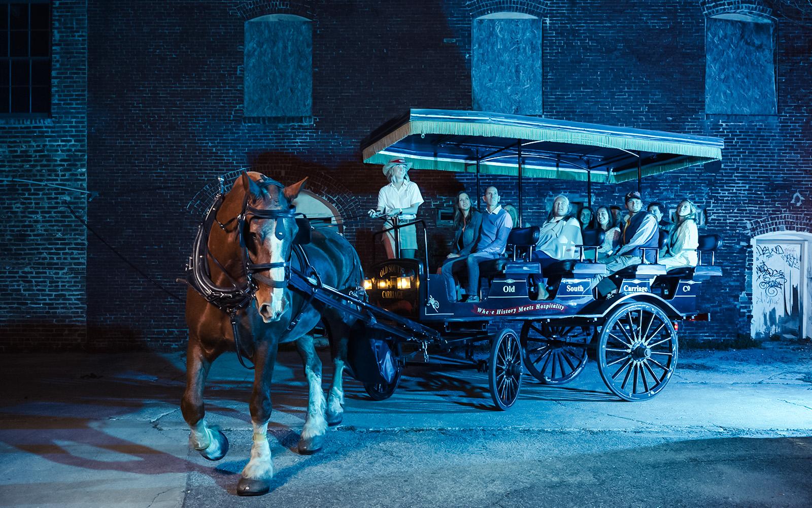 Charleston horse-drawn carriage tour at night with passengers and guide.