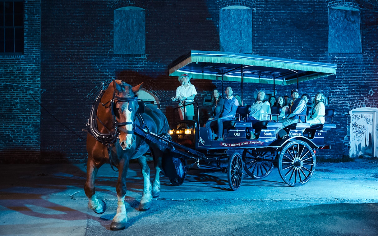 Charleston horse-drawn carriage tour at night with passengers and guide.
