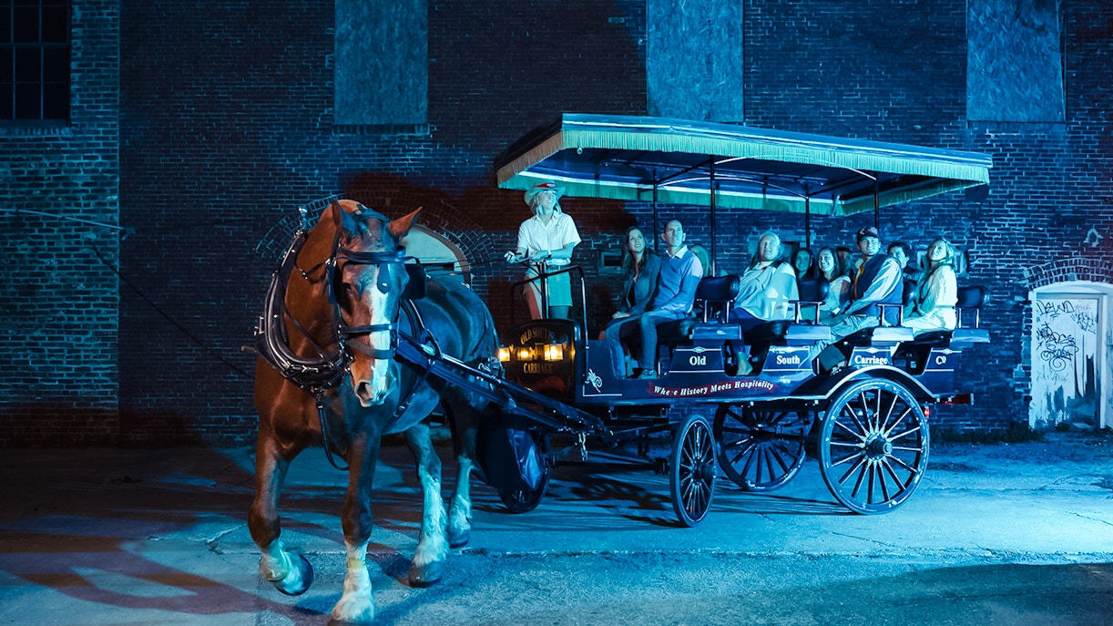 Charleston horse-drawn carriage tour at night with passengers and guide.