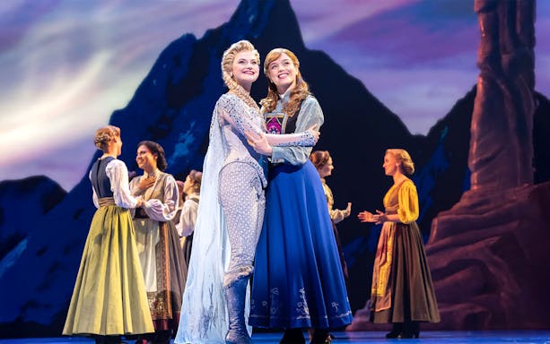 Musical scene from Disney FROZEN with characters on stage in front of a mountain backdrop.