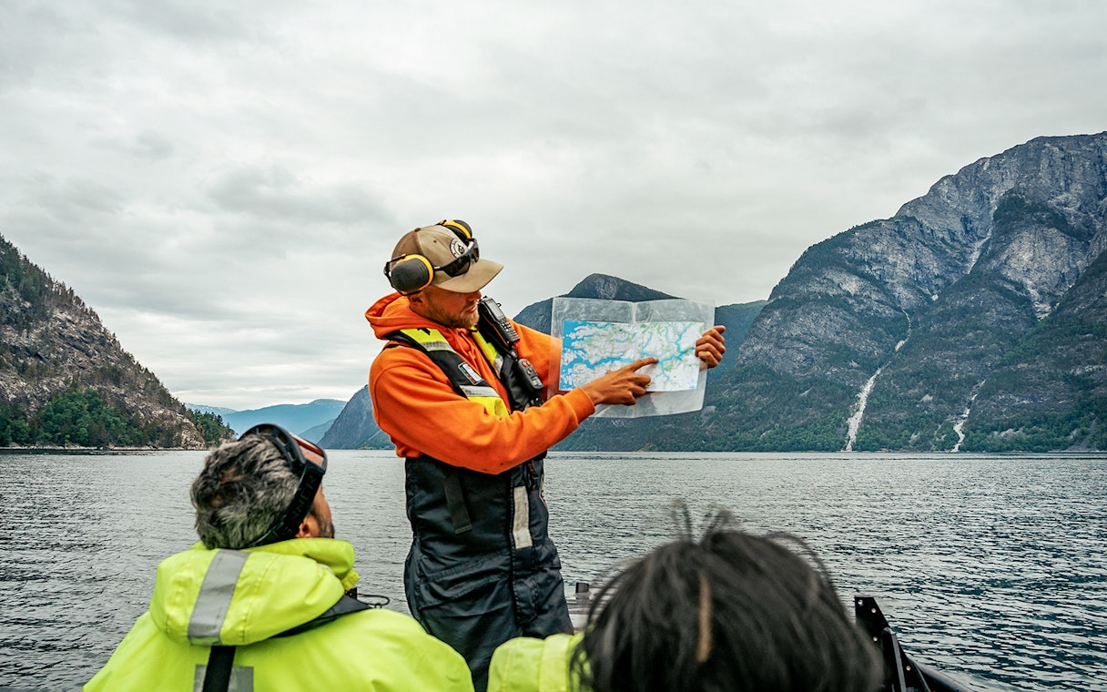 Guide showing map on RIB boat during Tromso whale safari with mountains in background.